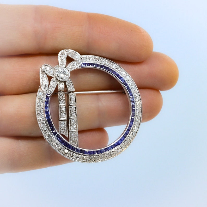 May include: A silver brooch with a diamond bow and a circle of sapphires and diamonds.