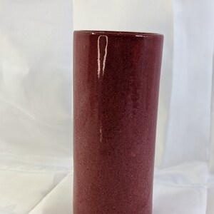Peut inclure: Un vase en céramique rouge foncé avec une surface texturée. Le vase est de forme cylindrique et a une finition lisse et brillante.