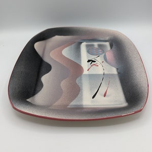 May include: A rectangular ceramic serving tray with a black, white, pink, and gray abstract design. The tray has a red rim.