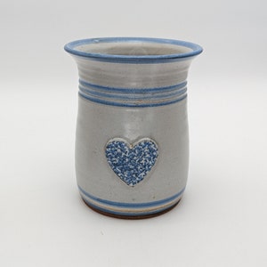 May include: A white ceramic vase with a blue heart design and blue stripes around the top and bottom.