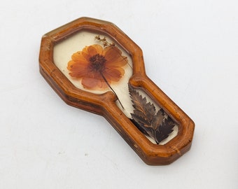 May include: A wooden key holder with a pressed flower and leaf design. The flower is orange and the leaf is green.