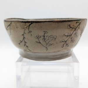 Könnte beinhalten: Eine kleine, cremefarbene Keramikschale mit schwarzem Blumenmuster. Die Schale hat einen leicht unebenen Rand und einen abgerundeten Boden.