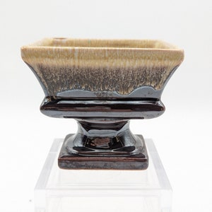 May include: A square ceramic planter with a brown and beige glaze. The planter has a pedestal base.