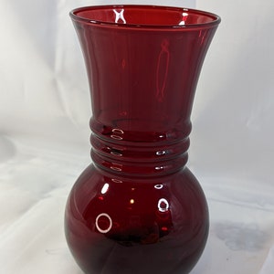 May include: A deep red glass vase with a round base and a flared top. The vase has a textured design around the middle.