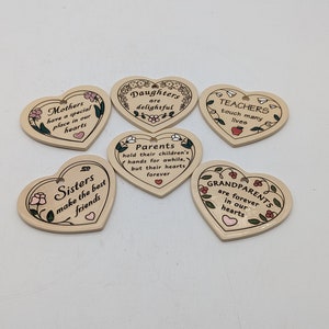 May include: Six heart-shaped ceramic ornaments with floral designs and inspirational messages. The messages include "Mothers have a special place in our hearts", "Daughters are delightful", "Teachers touch many lives", "Sisters make the best friends", "Parents hold their children's hands for awhile, but their hearts forever", and "Grandparents are forever in our hearts".