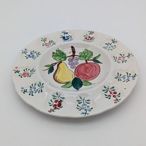 May include: A white ceramic egg plate with a floral design and a painted image of a pear, apple, and grapes in the center.