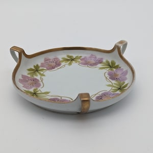 Puede incluir: Un plato de porcelana blanca con ribete dorado y un diseño floral. El plato tiene dos asas a cada lado.