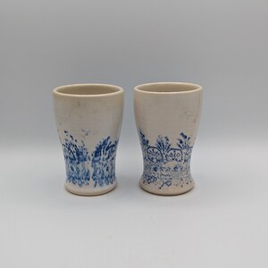 Peut inclure: Deux tasses en céramique blanche avec des motifs floraux bleus. Les tasses sont légèrement évasées en haut et en bas.
