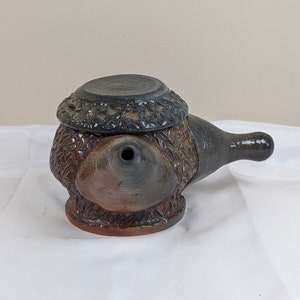 May include: A brown and black ceramic teapot with a lid and a spout. The teapot has a textured surface and a unique design.