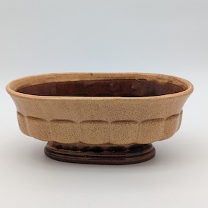 May include: A light brown oval ceramic planter with a fluted design around the rim and a brown base.