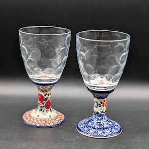 May include: Two clear wine glasses with patterned stems. One stem has a brown and red floral design, the other has a blue floral design. The glass bowls have a textured pattern.