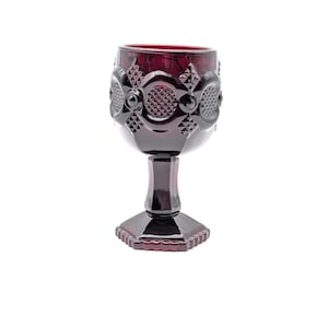 Könnte beinhalten: Ein rubinroter Kelch mit einem detaillierten, gemusterten Design um die Schale. Der Stiel und der Fuß sind ebenfalls rot, mit einem facettierten Fuß. Das Glas ist wahrscheinlich Vintage und eignet sich für die Präsentation oder den Gebrauch.