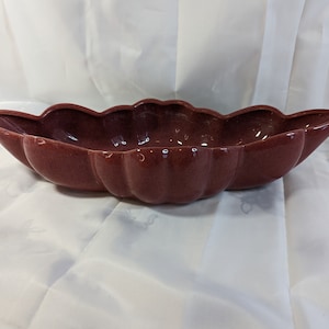 Könnte beinhalten: Eine große, rote Keramikschale mit einem gewellten Rand. Die Schale ist bootförmig und hat eine glatte, glänzende Oberfläche.