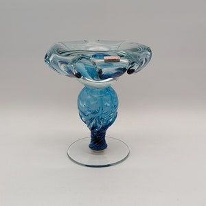 Pode incluir: Uma tigela de vidro azul em um pedestal com um design de redemoinho. A tigela está em uma base de vidro transparente.