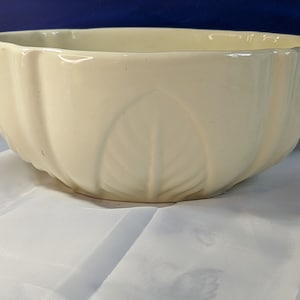 Könnte beinhalten: Eine weiße Keramikschüssel mit geriffeltem Design und Blattmotiv. Die Schüssel steht auf einer weißen Oberfläche.