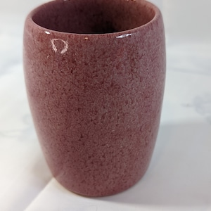 May include: A small, round, red ceramic cup with a textured surface.