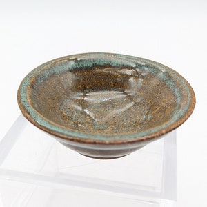 May include: A small, brown ceramic bowl with a green glaze. The bowl has a slightly textured surface and a rounded shape.