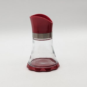 May include: A red glass bottle with a red plastic top and a silver band around the neck. The bottle has a wide base and a narrow neck.