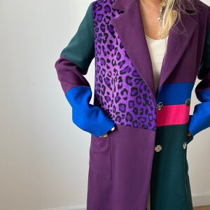 Peut inclure: Un long manteau violet, vert et bleu avec un panneau imprimé léopard. Le manteau a une fermeture à double boutonnage et deux poches.