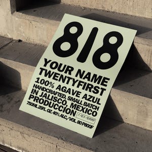 Op de afbeelding: Een lichtgroen rechthoekig bord met het nummer "818" in grote zwarte letters. Het bord heeft de tekst "YOUR NAME TWENTYFIRST 100% AGAVE AZUL HANDCRAFTED, SMALL BATCH IN JALISCO, MEXICO PRODUCCION".