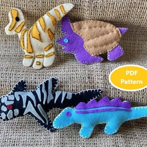 Könnte beinhalten: Vier Filztier-Spielzeuge: ein gelber und weißer Dinosaurier, ein lila und brauner Triceratops, ein schwarz-weißer Hai und ein blauer und lila Dinosaurier. Die Spielzeuge sind auf einem braunen Jutesack-Hintergrund angeordnet. PDF-Muster.