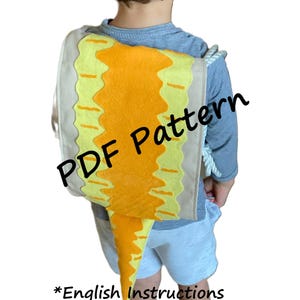 May include: A child wearing a yellow and brown dinosaur costume with a tail. The costume is a backpack with a tail that hangs down. The text "PDF Pattern" is superimposed on the image. The text "*English Instructions" is at the bottom of the image.