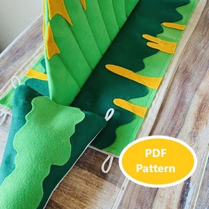 Könnte beinhalten: Eine handgefertigte Spielmatte aus Filz mit einem Bergdesign. Die Matte hat Grün- und Gelbtöne mit einer Bergkette und blattartigen Formen. Der Text "PDF Pattern" befindet sich in einem gelben Oval.