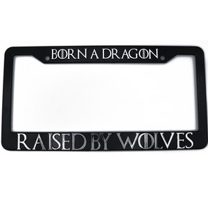 Puede incluir: Marco de matrícula negro con el texto "Born a Dragon, Raised by Wolves" en letras plateadas.