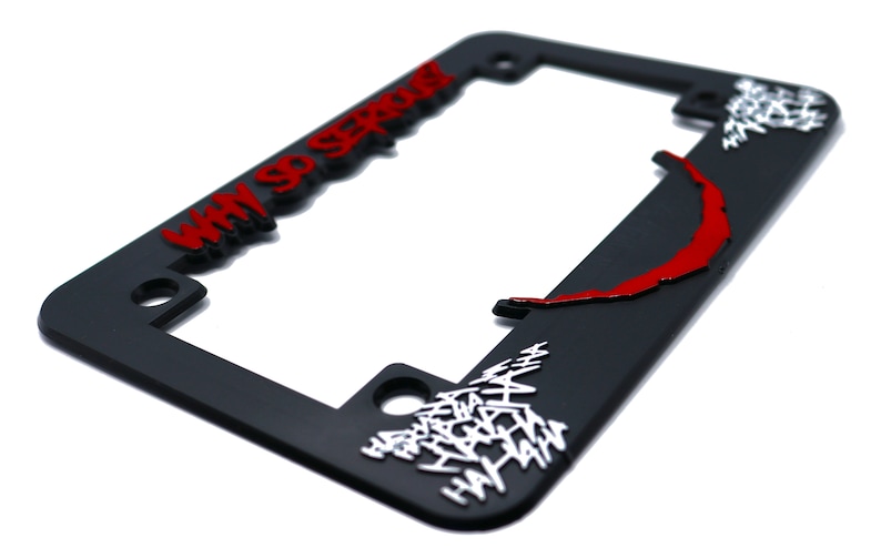 May include: Black plastic license plate frame with a red and white Joker design. The frame features the text "Why So Serious?" and a red Joker smile.