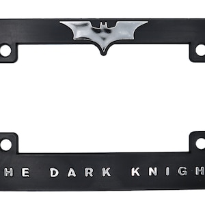 May include: Black license plate frame with the words "THE DARK KNIGHT" in silver lettering. A silver bat symbol is at the top center. The frame has four mounting holes.