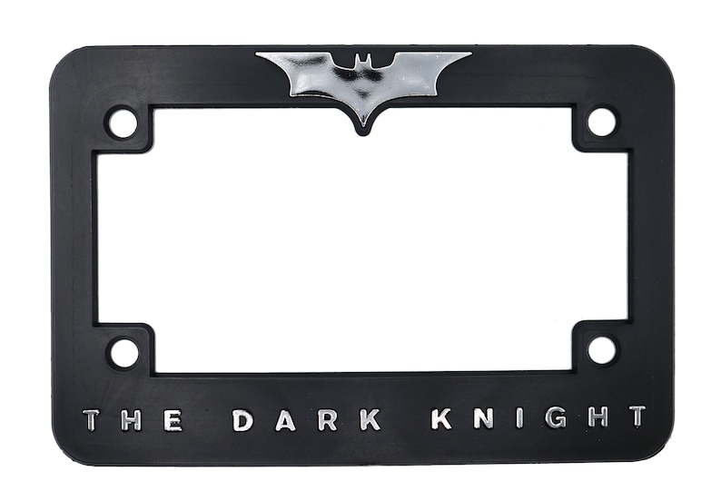May include: Black license plate frame with the words "THE DARK KNIGHT" in silver lettering. A silver bat symbol is at the top center. The frame has four mounting holes.