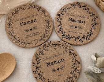 May include: Three round cork coasters featuring a black printed design of a floral wreath, hearts, and the text "Les bons petits plats de Maman" along with various names including Kevin, Laurine, Florian, Mathieu, Claire, and Emma printed below.