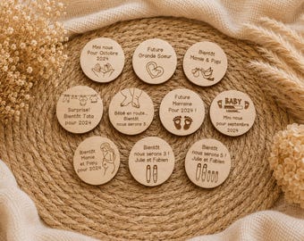 May include: A collection of ten circular wooden discs featuring various laser-engraved illustrations and French text related to pregnancy announcements, including depictions of baby feet, a stork, a pregnant silhouette, and baby clothing on a line.