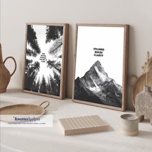 May include: Two framed wall art prints in wooden frames. The left print shows a low-angle view of pine trees with the text KEEP MOVING FORWARD, ONE STEP AT A TIME. The right print shows a mountain peak with the text STILLNESS BUILDS CLARITY.