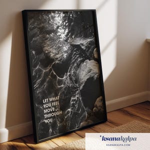 May include: A black framed wall art print featuring a high-contrast black and white photograph of water flowing over dark rocks. The image displays light reflections on the water surface and includes the white text: LET WHAT YOU FEEL MOVE THROUGH YOU.