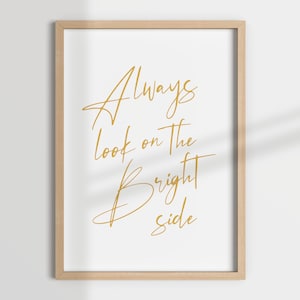 Può includere: Stampa incorniciata con la scritta dorata "Always look on the bright side" su sfondo bianco. La cornice è in legno chiaro. Il design è minimalista e motivazionale.