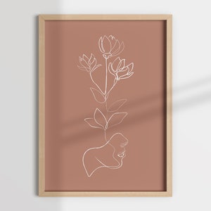 May include: A minimalist line art print featuring a single flower with a face in the stem. The print is on a terracotta background and framed in a light wood frame.