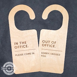 Puede incluir: Dos colgadores de puerta de madera con un gancho en la parte superior. El colgador de la izquierda dice "En la oficina. Por favor, entre." El colgador de la derecha dice "Fuera de la oficina. Lo siento, me perdí."