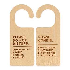 May include: Two light-coloured wooden door hangers with dark brown text. The left hanger reads: PLEASE DO NOT DISTURB. UNLESS YOU'RE: 1. DYING 2. ON FIRE 3. A PUPPY. The right hanger reads: PLEASE COME IN. EVEN IF YOU'RE: 1. NOT DYING 2. NOT ON FIRE 3. NOT A PUPPY.