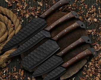 Puede incluir: Un juego de seis cuchillos de cocina negros con hojas texturizadas y mangos de madera oscura. Los cuchillos están colocados sobre una superficie de madera con virutas y una cuerda en el fondo. Las hojas tienen una textura martillada.