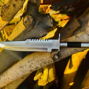 May include: A stainless steel knife with a serrated spine and a black handle. The blade is sharp and reflective, with a silver finish. The knife is designed for outdoor use and survival.