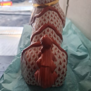 May include: A ceramic dog figurine with a red and white pattern. The dog has a gold collar and a red tail. The figurine is sitting on a blue surface.