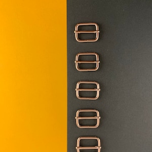 Può includere: Cinque fibbie scorrevoli in metallo dorato disposte verticalmente su uno sfondo nero e giallo.