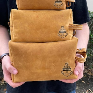 May include: Three brown leather toiletry bags with an anchor and the name "ROBERT" embossed on each bag.