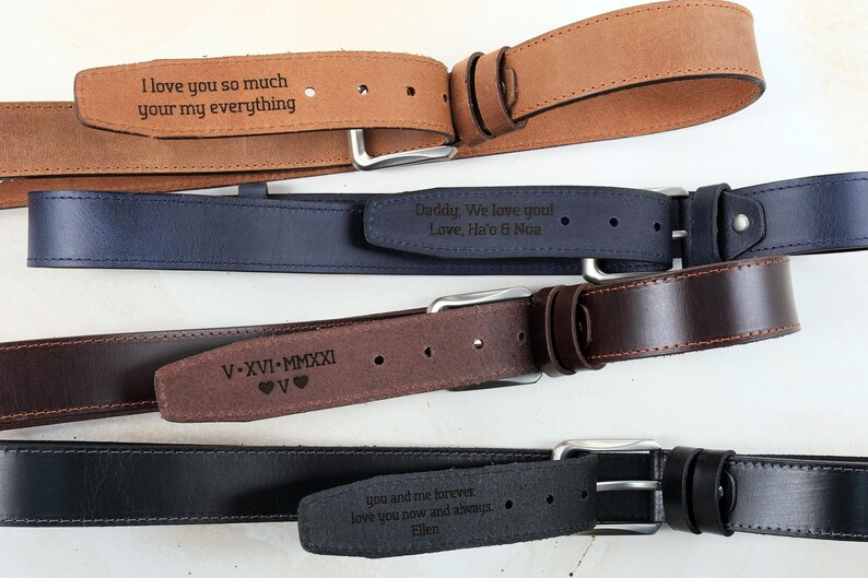 May include: Four leather belts in tan, navy blue, dark brown, and black, each featuring a silver-toned metal buckle and a personalised laser-engraved message on the strap. The engravings include text such as I love you so much, V-XVI-MMXXI, and more.