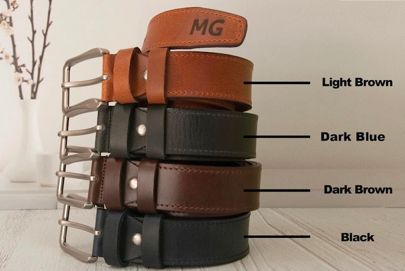 May include: A stack of four leather belts with silver-toned metal buckles, featuring colours labelled as Light Brown, Dark Blue, Dark Brown, and Black. The top light brown belt is engraved with the letters MG. Each belt has a single metal rivet.