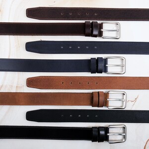 May include: A collection of four leather belts in dark brown, navy blue, tan, and black. Each belt features a smooth finish, a rectangular silver-toned metal buckle, two matching leather keepers, and a series of punched holes for adjustment.