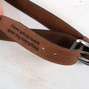 May include: A brown suede belt featuring a silver-toned metal buckle and a laser-engraved message on the inner strap that reads, I love you so much your my everything. The belt includes evenly spaced adjustment holes along the length of the strap.