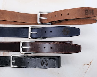 May include: Four leather belts with silver-toned metal buckles arranged horizontally. The top belt is tan with the letters BH, the second is navy blue with an S, the third is dark brown, and the bottom is black with a K inside a laurel wreath.