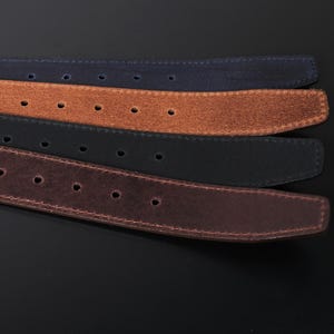 May include: A set of four belts in navy blue, tan, black, and dark brown. Each belt features a textured suede-like finish, visible stitching along the edges, and a series of evenly spaced circular adjustment holes running along the length of the strap.